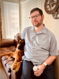 dog, dog training,man in blue button up shirt sittign on couch with a german shepherd dog leaning on his side
